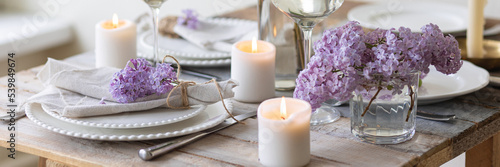 Beautiful table decor for a wedding dinner with a spring blooming lilac flowers. Celebration of a special event. Fancy white plates, and wineglasses. Countryside style. Banner