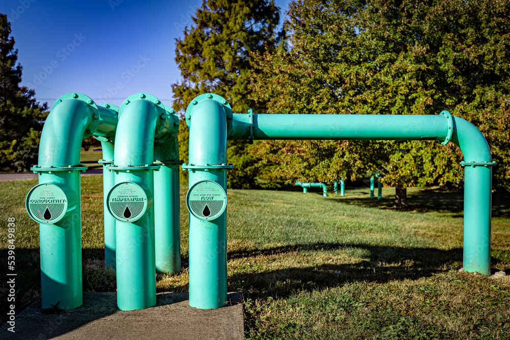 Teal colored pipes coming out of the ground in a park lawn. Their