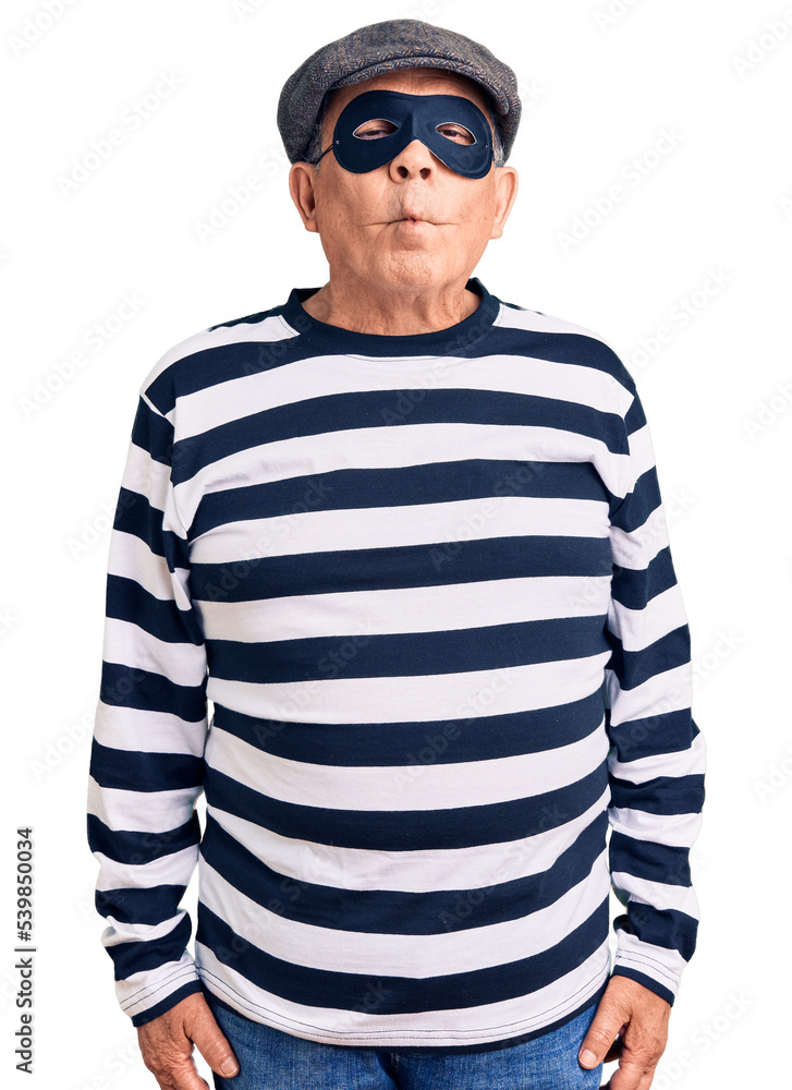 Senior handsome man wearing burglar mask and t-shirt making fish face with lips, crazy and comical gesture. funny expression. Senior handsome man wearing burglar mask and t-shirt making fish face with lips, crazy and comical gesture. funny expression.