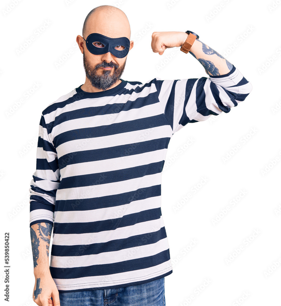 Young handsome man wearing burglar mask strong person showing arm muscle, confident and proud of power Young handsome man wearing burglar mask strong person showing arm muscle, confident and proud of power