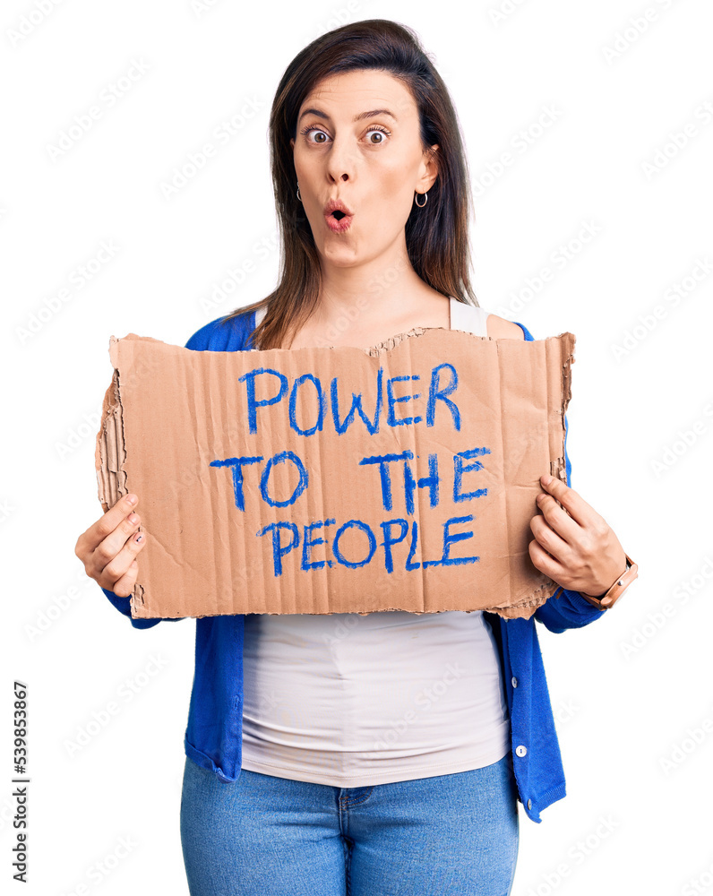 Young beautiful woman holding power to the people banner scared and amazed with open mouth for surprise, disbelief face Young beautiful woman holding power to the people banner scared and amazed with open mouth for surprise, disbelief face
