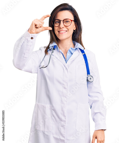 Young beautiful woman wearing doctor stethoscope and glasses smiling and confident gesturing with hand doing small size sign with fingers looking and the camera. measure concept.