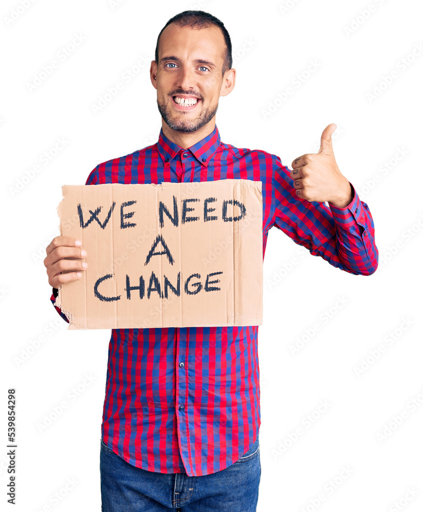 Young handsome man holding we need a change banner smiling happy and positive, thumb up doing excellent and approval sign Young handsome man holding we need a change banner smiling happy and positive, thumb up doing excellent and approval sign