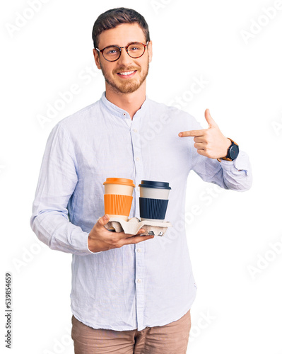 Handsome young man with bear holding takeaway cup of coffee pointing finger to one self smiling happy and proud