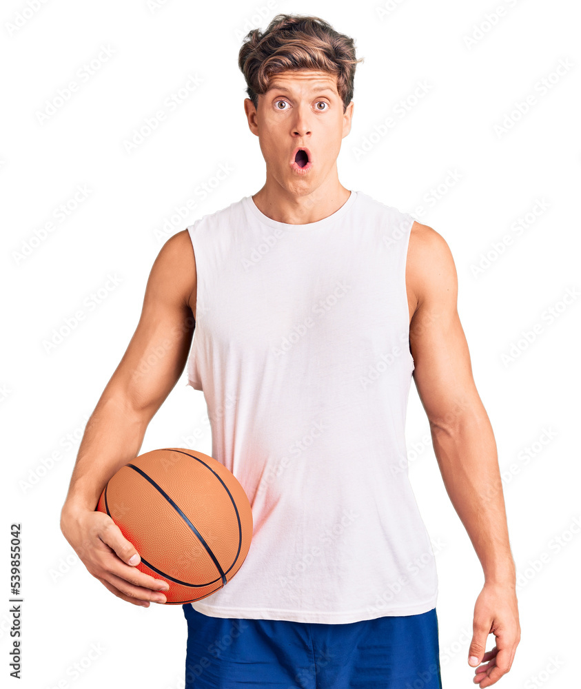 Young handsome man holding basketball ball scared and amazed with open mouth for surprise, disbelief face Young handsome man holding basketball ball scared and amazed with open mouth for surprise, disbelief face