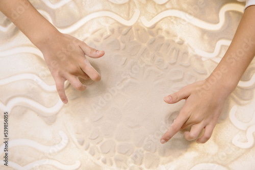 The child draws with fingers on the light table with quartz sand to develop motor skills