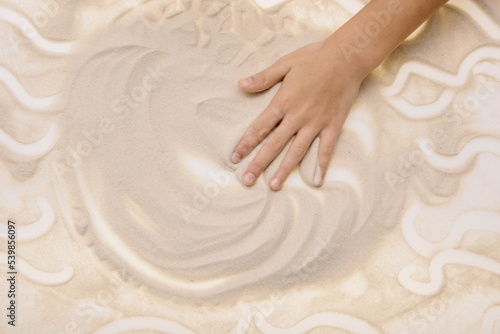 The child draws with fingers on the light table with quartz sand to develop motor skills