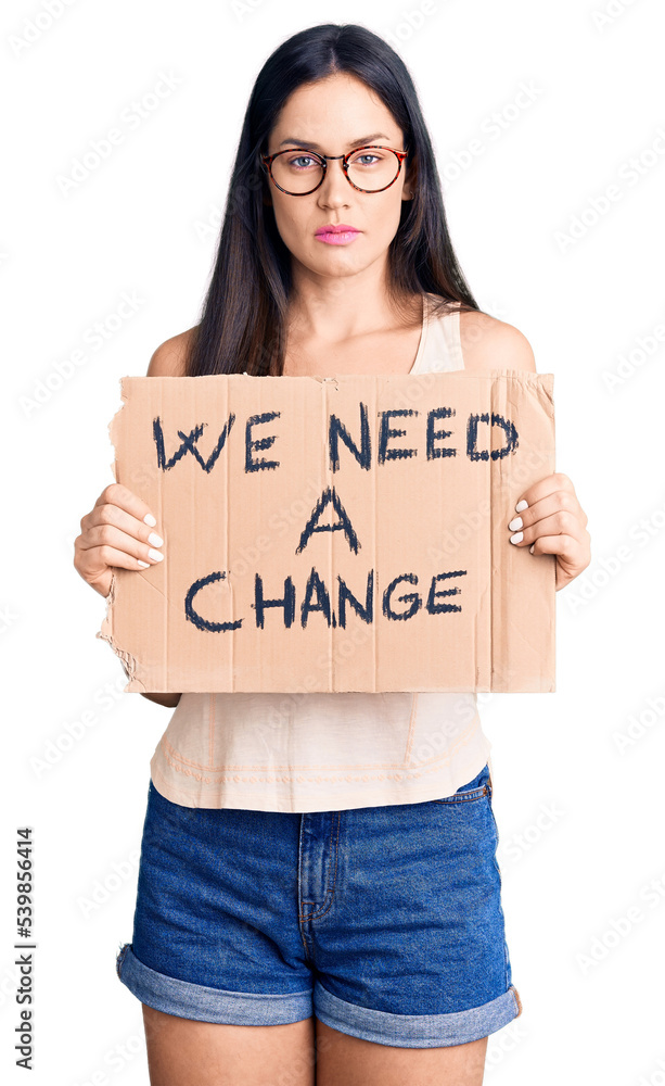 Young beautiful caucasian woman holding we need a change banner thinking attitude and sober expression looking self confident Young beautiful caucasian woman holding we need a change banner thinking attitude and sober expression looking self confident