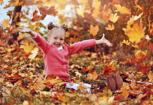 Happy girl sitting on the ground throwing autumn leafs in the air