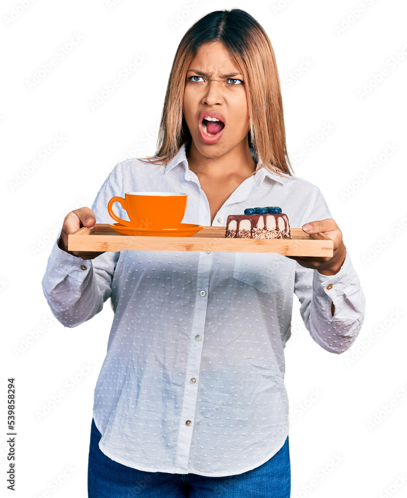 Young hispanic woman holding tray with coffee and cake angry and mad screaming frustrated and furious, shouting with anger. rage and aggressive concept. Young hispanic woman holding tray with coffee and cake angry and mad screaming frustrated and furious, shouting with anger. rage and aggressive concept.