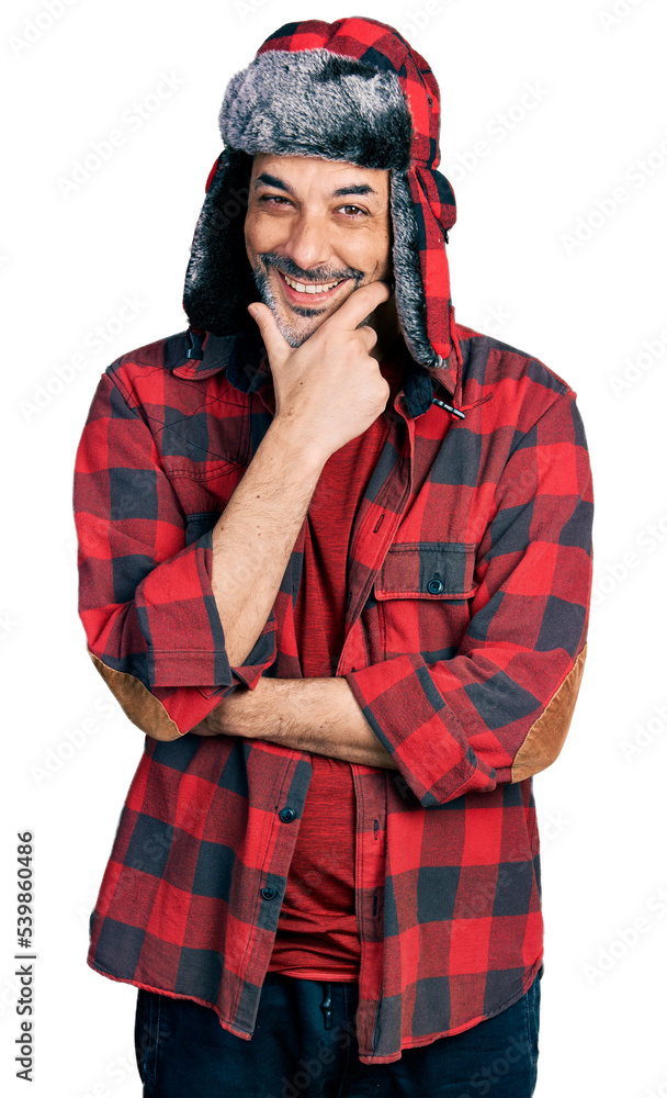 Middle age hispanic man with grey hair wearing fluffy earmuff hat looking confident at the camera smiling with crossed arms and hand raised on chin. thinking positive. Middle age hispanic man with grey hair wearing fluffy earmuff hat looking confident at the camera smiling with crossed arms and hand raised on chin. thinking positive.
