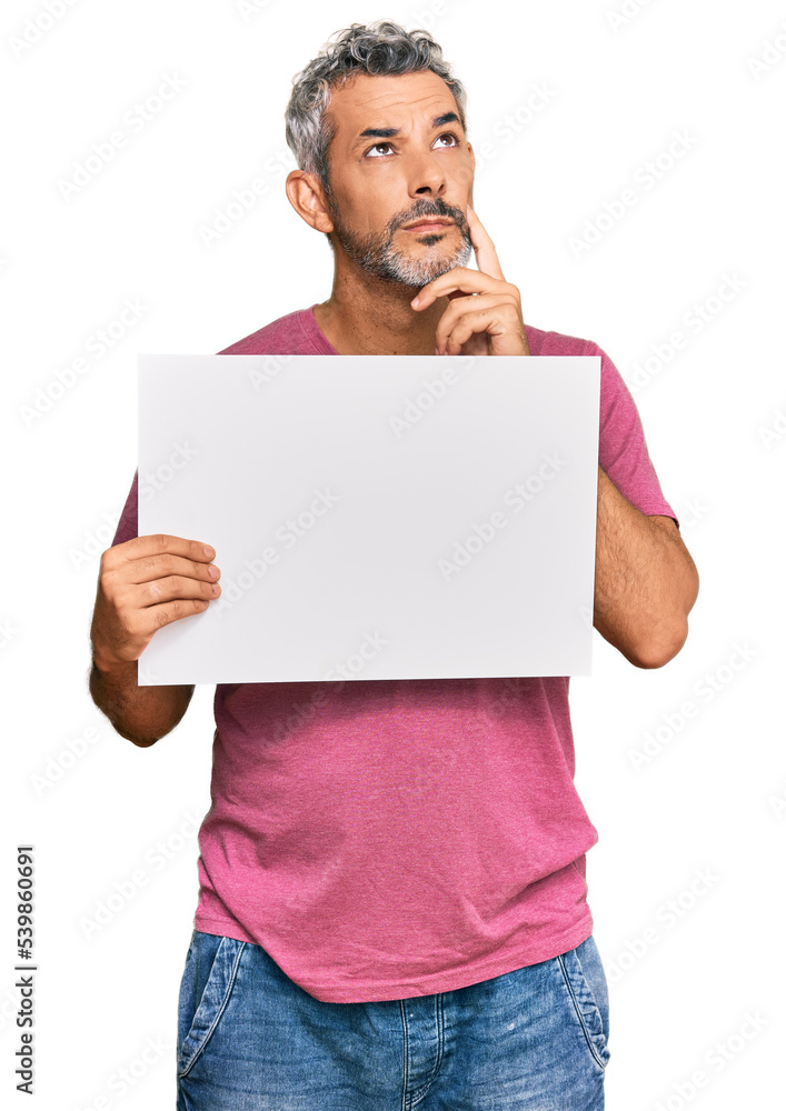 Middle age grey-haired man holding blank empty banner serious face thinking about question with hand on chin, thoughtful about confusing idea Middle age grey-haired man holding blank empty banner serious face thinking about question with hand on chin, thoughtful about confusing idea