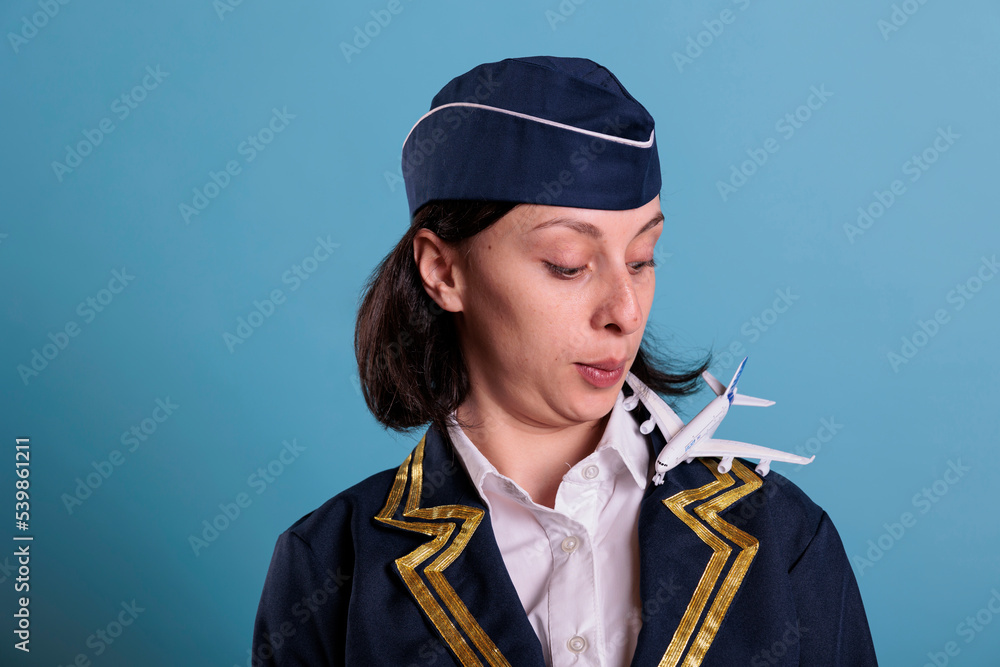 Flight attendant looking ar airplane model landing on shoulder, aviation academy stewardess playing with plane. Air hostess in professional uniform with jet toy, medium close up Flight attendant looking ar airplane model landing on shoulder, aviation academy stewardess playing with plane. Air hostess in professional uniform with jet toy, medium close up