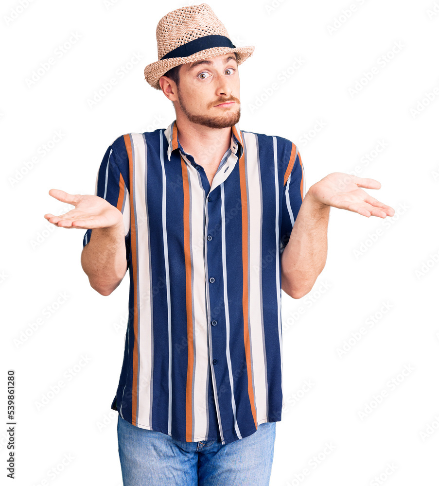 Young handsome caucasian man wearing summer hat clueless and confused expression with arms and hands raised. doubt concept. Young handsome caucasian man wearing summer hat clueless and confused expression with arms and hands raised. doubt concept.