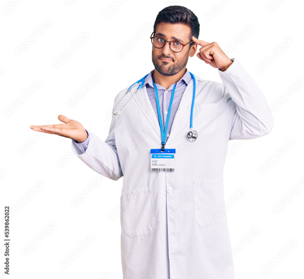Young hispanic man wearing doctor uniform and stethoscope confused and annoyed with open palm showing copy space and pointing finger to forehead. think about it. Young hispanic man wearing doctor uniform and stethoscope confused and annoyed with open palm showing copy space and pointing finger to forehead. think about it.
