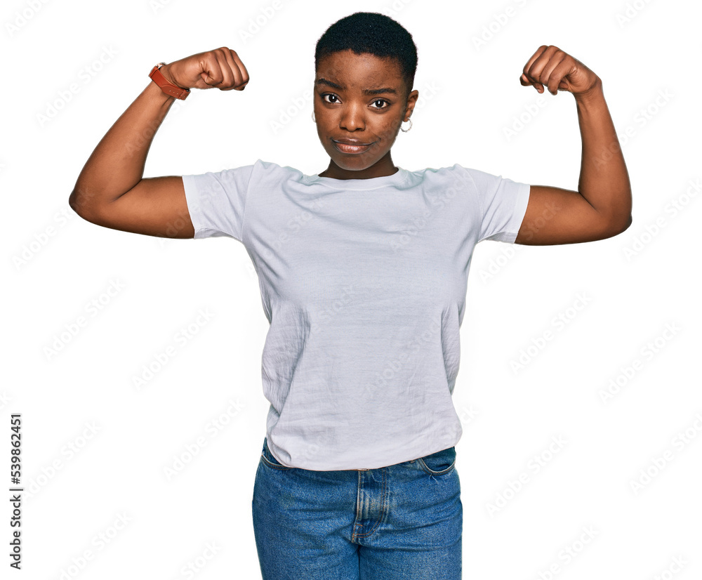 Young african american woman wearing casual white t shirt showing arms muscles smiling proud. fitness concept. Young african american woman wearing casual white t shirt showing arms muscles smiling proud. fitness concept.