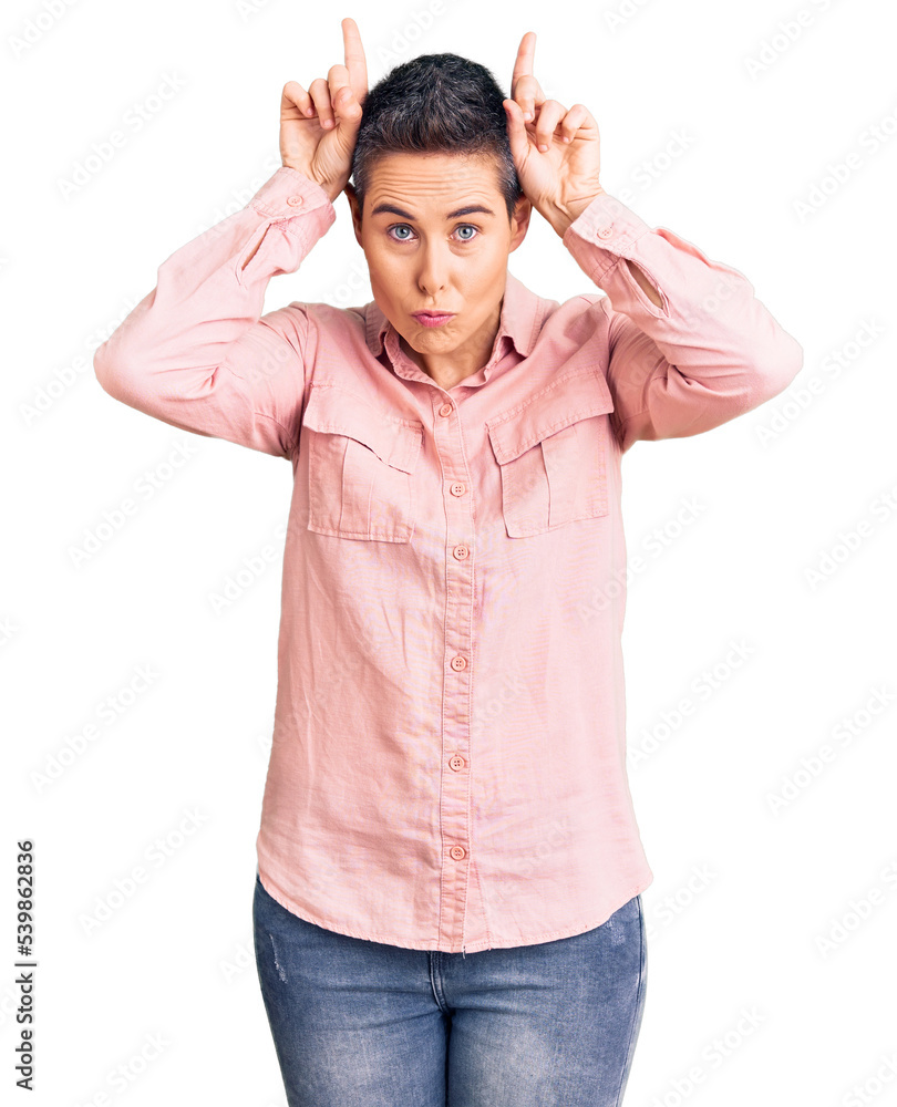 Naklejka premium Young woman with short hair wearing casual clothes doing funny gesture with finger over head as bull horns