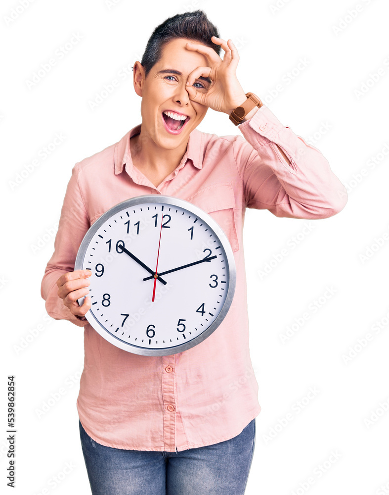 Young woman with short hair holding big clock smiling happy doing ok sign with hand on eye looking through fingers Young woman with short hair holding big clock smiling happy doing ok sign with hand on eye looking through fingers
