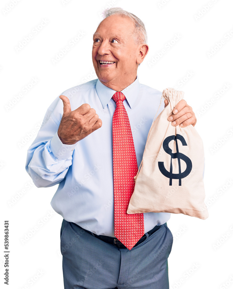 Senior handsome grey-haired man wearing elegant clothes holding money bag pointing thumb up to the side smiling happy with open mouth Senior handsome grey-haired man wearing elegant clothes holding money bag pointing thumb up to the side smiling happy with open mouth