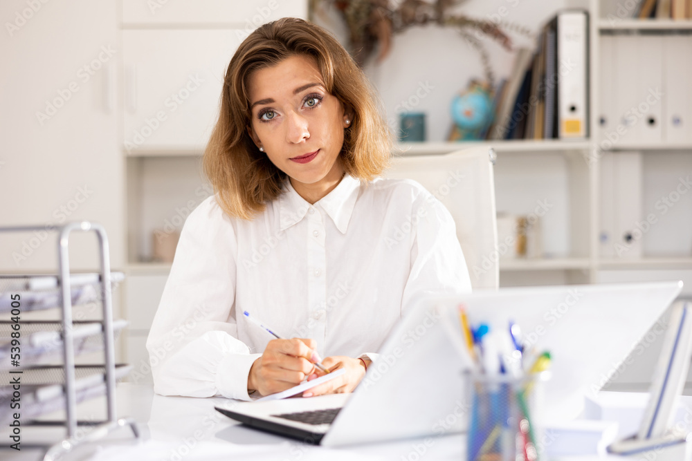 Woman bookkeeper sitting at table in her workplace and writing on paper.