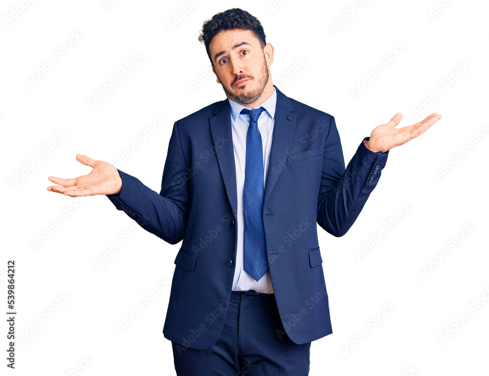 Young hispanic man wearing business clothes clueless and confused expression with arms and hands raised. doubt concept. Young hispanic man wearing business clothes clueless and confused expression with arms and hands raised. doubt concept.