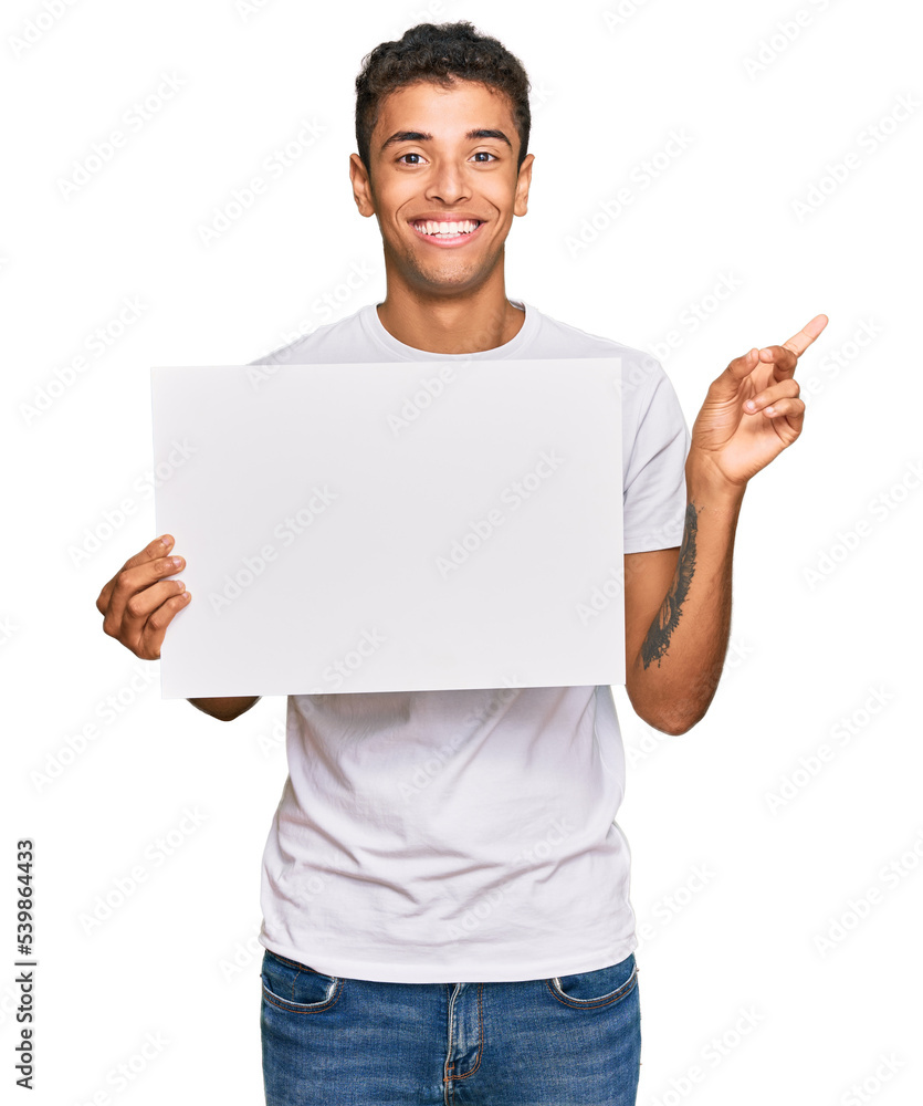 Young handsome african american man holding blank empty banner smiling happy pointing with hand and finger to the side Young handsome african american man holding blank empty banner smiling happy pointing with hand and finger to the side