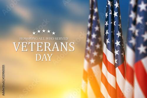 American flags with Text Veterans Day Honoring All Who Served on sunset background. American holiday banner.