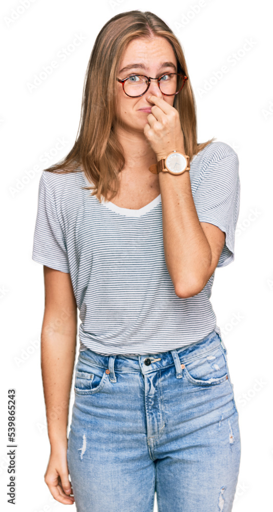 Beautiful young blonde woman wearing casual clothes and glasses smelling something stinky and disgusting, intolerable smell, holding breath with fingers on nose. bad smell Beautiful young blonde woman wearing casual clothes and glasses smelling something stinky and disgusting, intolerable smell, holding breath with fingers on nose. bad smell