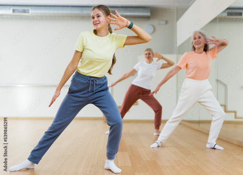 Portrait of cheerful active young girl exercising dance moves in fitness studio