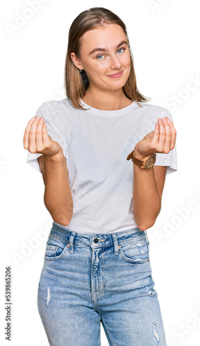 Beautiful young blonde woman wearing casual white t shirt doing money gesture with hands, asking for salary payment, millionaire business