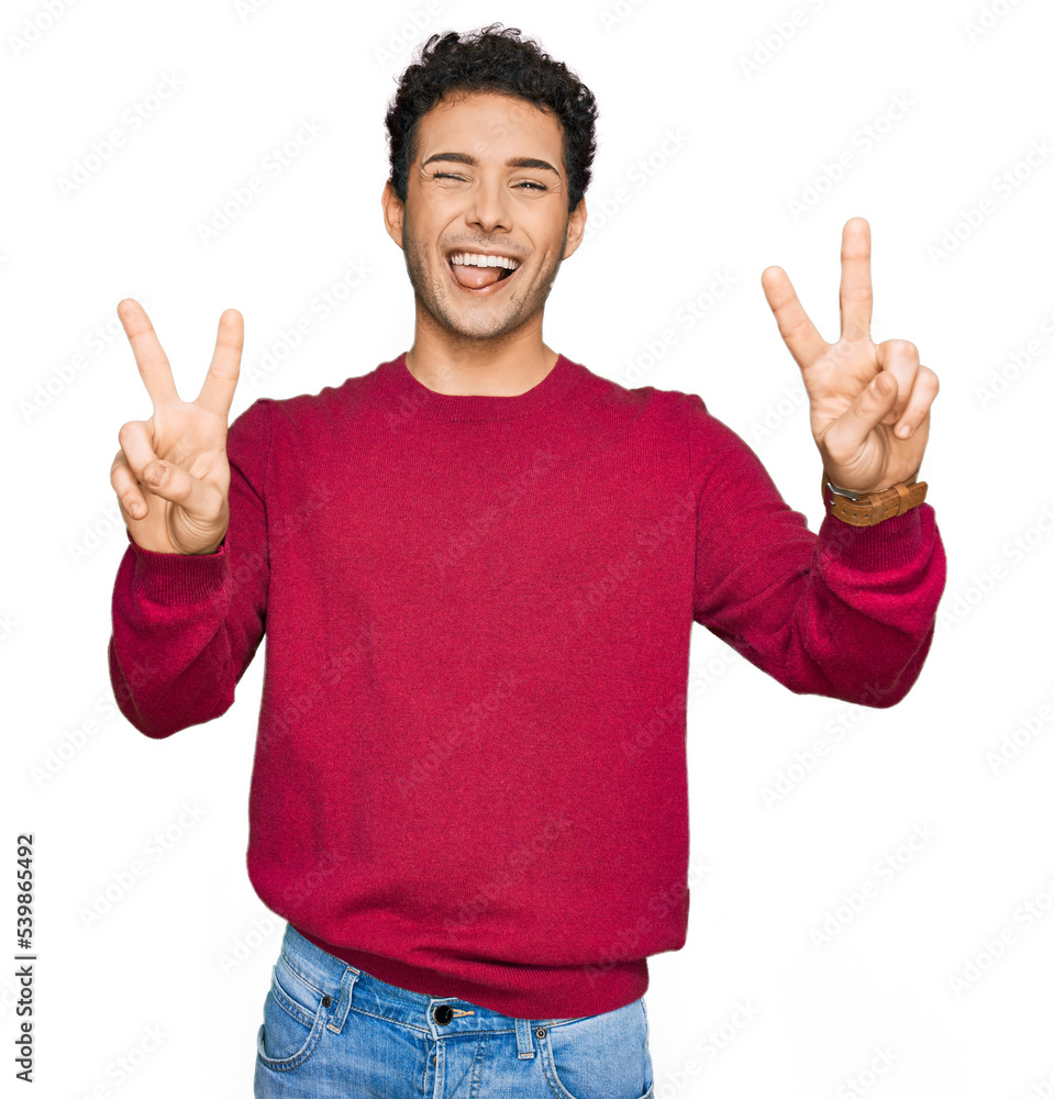 Fototapeta premium Young handsome man wearing casual clothes smiling with tongue out showing fingers of both hands doing victory sign. number two.