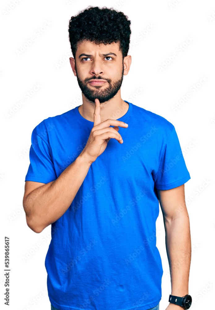 Young arab man with beard wearing casual blue t shirt thinking concentrated about doubt with finger on chin and looking up wondering Young arab man with beard wearing casual blue t shirt thinking concentrated about doubt with finger on chin and looking up wondering