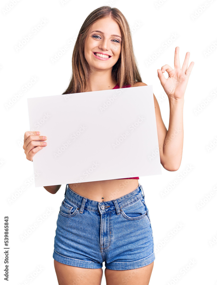 Young beautiful blonde woman holding blank empty banner doing ok sign with fingers, smiling friendly gesturing excellent symbol Young beautiful blonde woman holding blank empty banner doing ok sign with fingers, smiling friendly gesturing excellent symbol