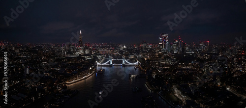 Photography Aerial view to the illuminated Tower Bridge and skyline of London, UK, just after sunset at night time