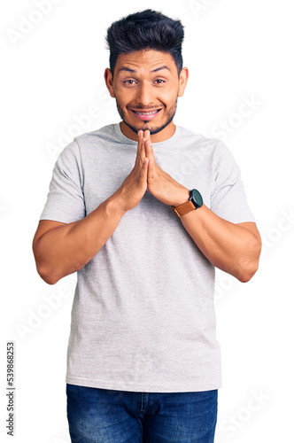 Handsome latin american young man wearing casual tshirt praying with hands together asking for forgiveness smiling confident.