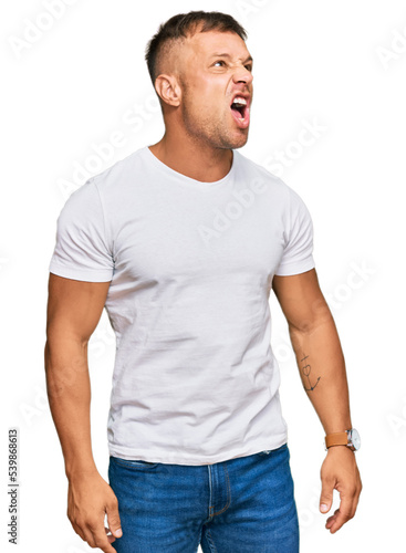 Handsome muscle man wearing casual white tshirt angry and mad screaming frustrated and furious  shouting with anger. rage and aggressive concept.