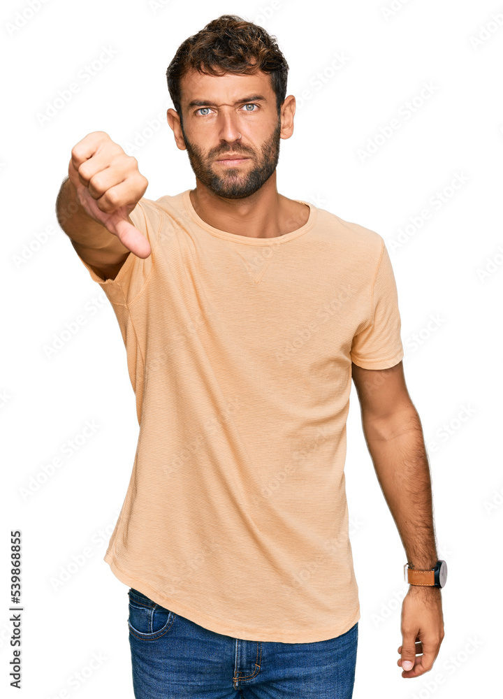 Handsome young man with beard wearing casual tshirt looking unhappy and angry showing rejection and negative with thumbs down gesture. bad expression. Handsome young man with beard wearing casual tshirt looking unhappy and angry showing rejection and negative with thumbs down gesture. bad expression.