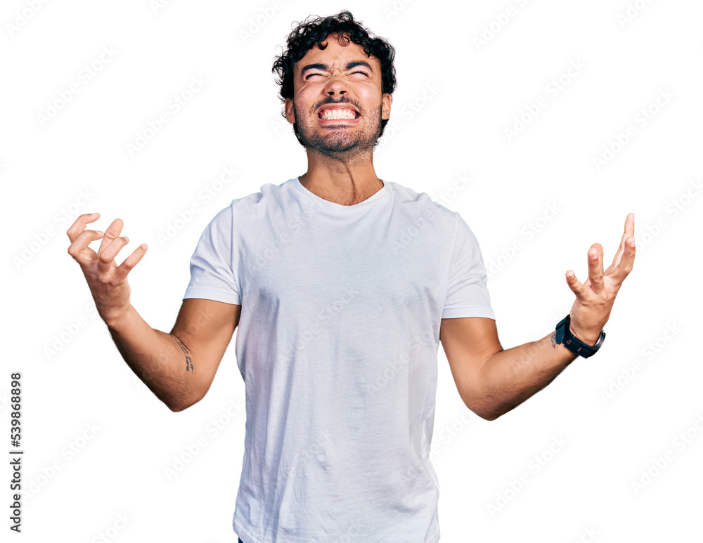 Hispanic young man with beard wearing casual white t shirt crazy and mad shouting and yelling with aggressive expression and arms raised. frustration concept. Hispanic young man with beard wearing casual white t shirt crazy and mad shouting and yelling with aggressive expression and arms raised. frustration concept.