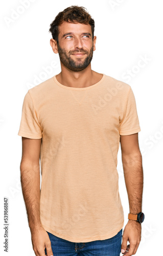 Handsome young man with beard wearing casual tshirt smiling looking to the side and staring away thinking.