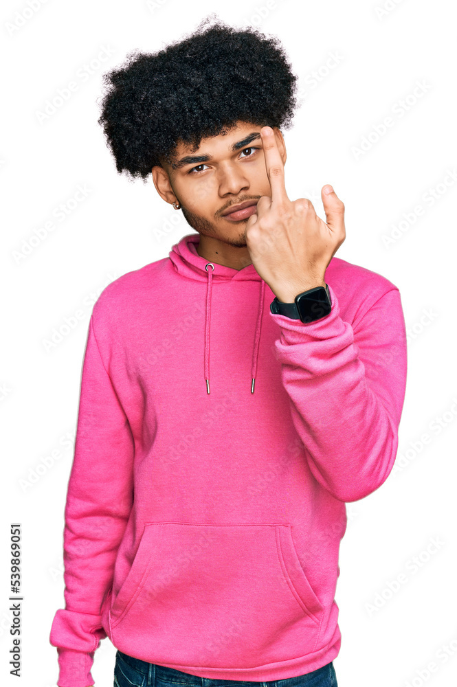 Young african american man with afro hair wearing casual pink sweatshirt showing middle finger, impolite and rude fuck off expression Young african american man with afro hair wearing casual pink sweatshirt showing middle finger, impolite and rude fuck off expression
