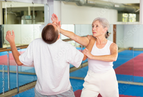 Senior European woman learning chin strike move on man during self-defense training.