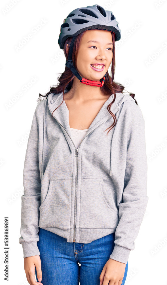 Young beautiful chinese girl wearing bike helmet looking away to side with smile on face, natural expression. laughing confident. Young beautiful chinese girl wearing bike helmet looking away to side with smile on face, natural expression. laughing confident.