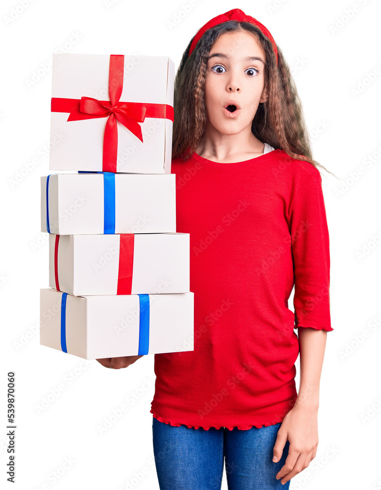 Cute hispanic child girl holding gift scared and amazed with open mouth for surprise, disbelief face Cute hispanic child girl holding gift scared and amazed with open mouth for surprise, disbelief face
