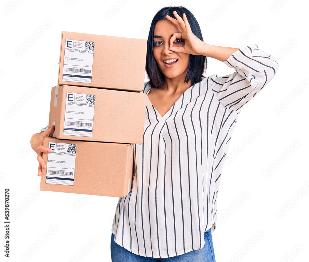 Young beautiful latin woman holding delivery package smiling happy doing ok sign with hand on eye looking through fingers Young beautiful latin woman holding delivery package smiling happy doing ok sign with hand on eye looking through fingers