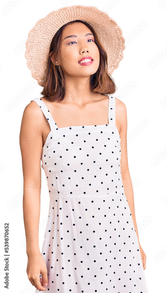Young beautiful chinese girl wearing summer hat looking away to side with smile on face, natural expression. laughing confident. Young beautiful chinese girl wearing summer hat looking away to side with smile on face, natural expression. laughing confident.