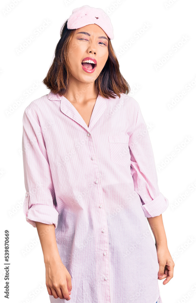 Young beautiful chinese girl wearing sleep mask and pajama winking looking at the camera with sexy expression, cheerful and happy face. Young beautiful chinese girl wearing sleep mask and pajama winking looking at the camera with sexy expression, cheerful and happy face.