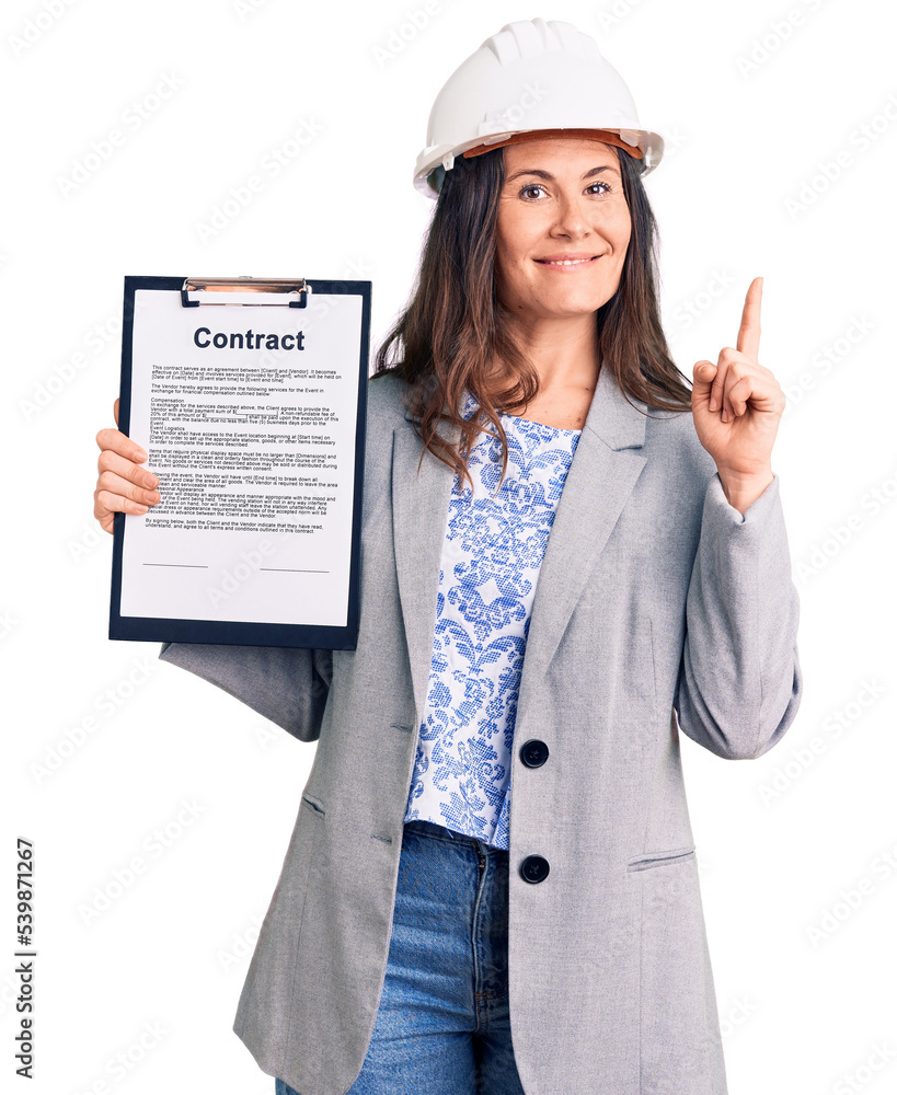 Young beautiful brunette woman wearing architect hardhat holding contract surprised with an idea or question pointing finger with happy face, number one Young beautiful brunette woman wearing architect hardhat holding contract surprised with an idea or question pointing finger with happy face, number one