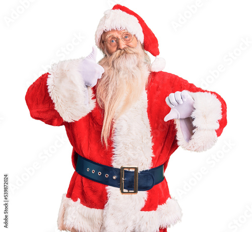 Old senior man with grey hair and long beard wearing traditional santa claus costume doing thumbs up and down, disagreement and agreement expression. crazy conflict
