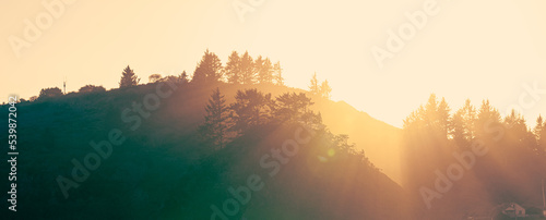 Wide shot of the sunrise over the mountains with light rays casting beautiful lines through the misty coastal air