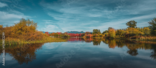 Colorful autumn landscape with mirror-like lake and spatters of trees in the midst of changing color